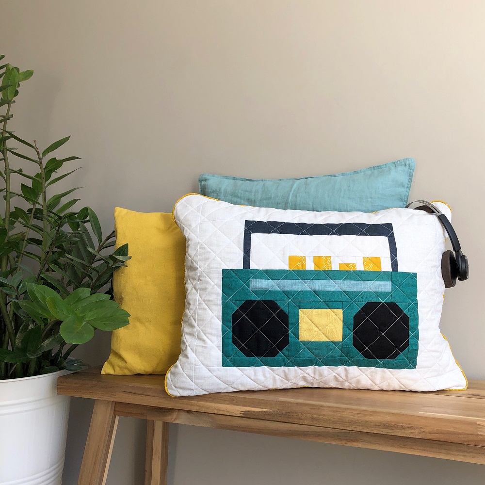Press Play quilt block finished as pillow cover, displayed on wooden bench