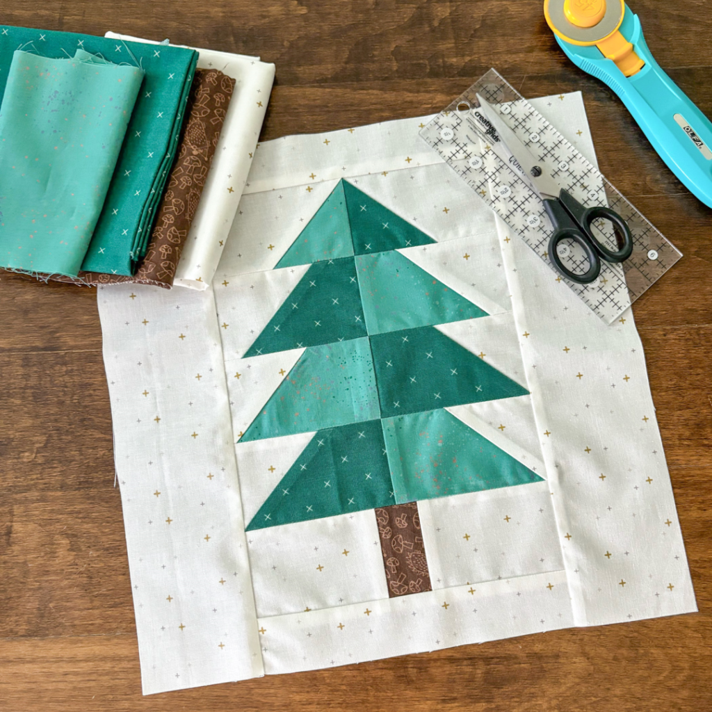 Apples & Beavers: unfinished Evergreen quilt block, fabric and quilting tools on hardwood floor